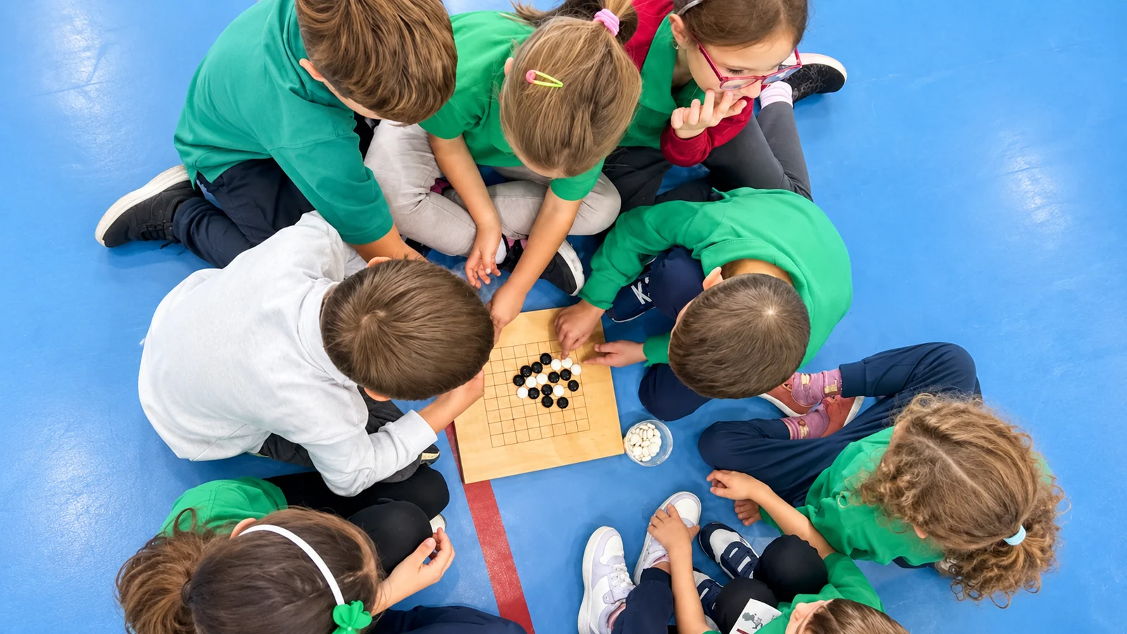 Elevi în tricouri verzi adunați în jurul unei table de Go